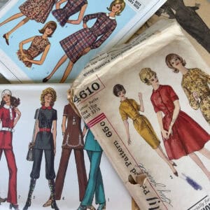 Vintage sewing pattern envelopes and booklets featuring illustrated women modeling 1960s and 1970s fashion styles, including dresses, skirts, and pants, in various colors and prints.