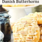 A close-up of Danish butterhorn pastries topped with white icing and almond slices, with a mug and a bowl in the background. Text above reads, “How To Make Danish Butterhorns.”.
