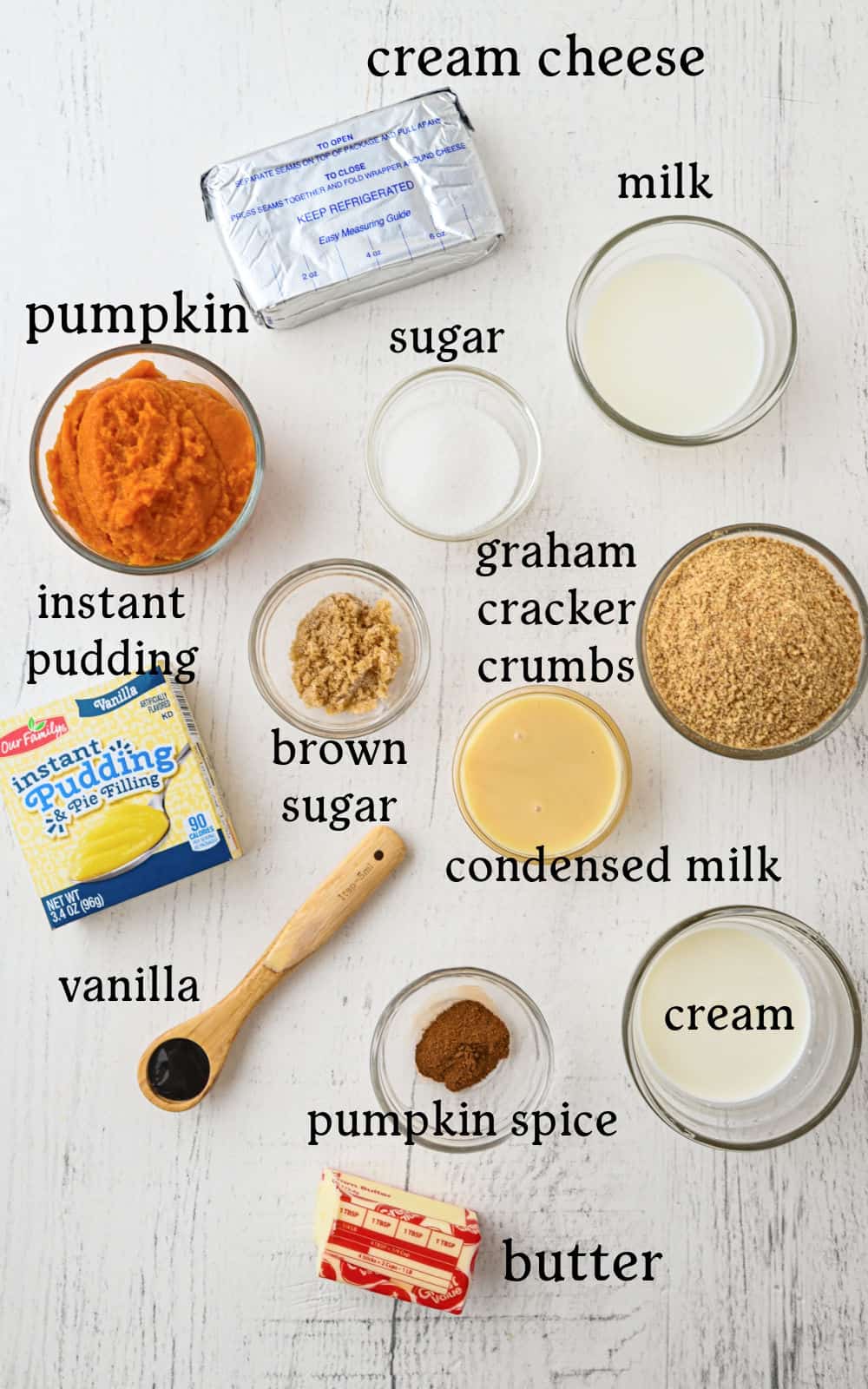 Ingredients for dessert arranged on a white surface: cream cheese, milk, pumpkin, sugar, instant pudding, brown sugar, graham cracker crumbs, condensed milk, cream, vanilla, pumpkin spice, and butter.